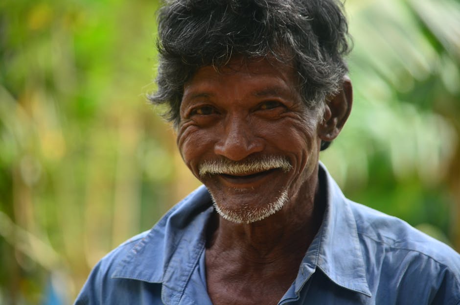 A cheerful senior man with a mustache smiling outdoors on a sunny day.