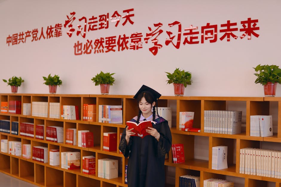 Female graduate in academic robe reading in a library with motivational Chinese text on the wall.