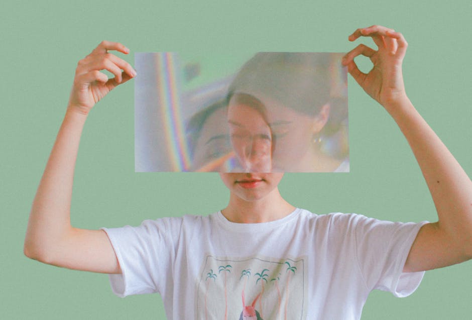 Artistic portrait of a woman holding a reflective surface, creating a double image effect indoors.