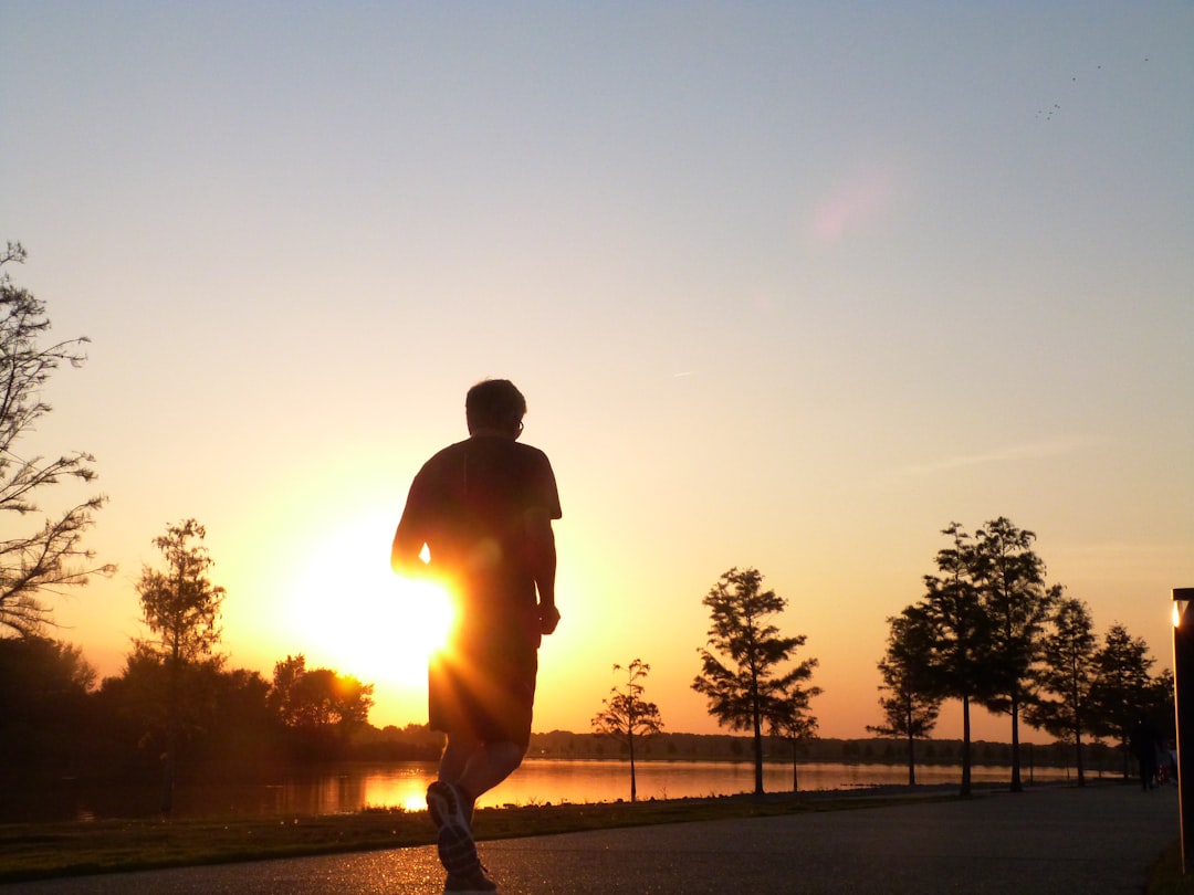 man in brown jacket and black pants walking on sidewalk during sunset
