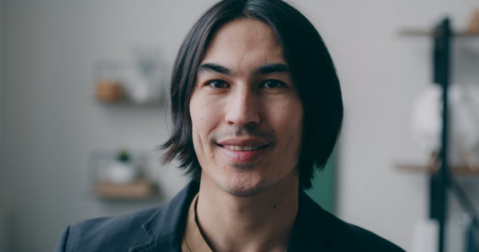 Close-up portrait of a smiling man with long hair indoors.