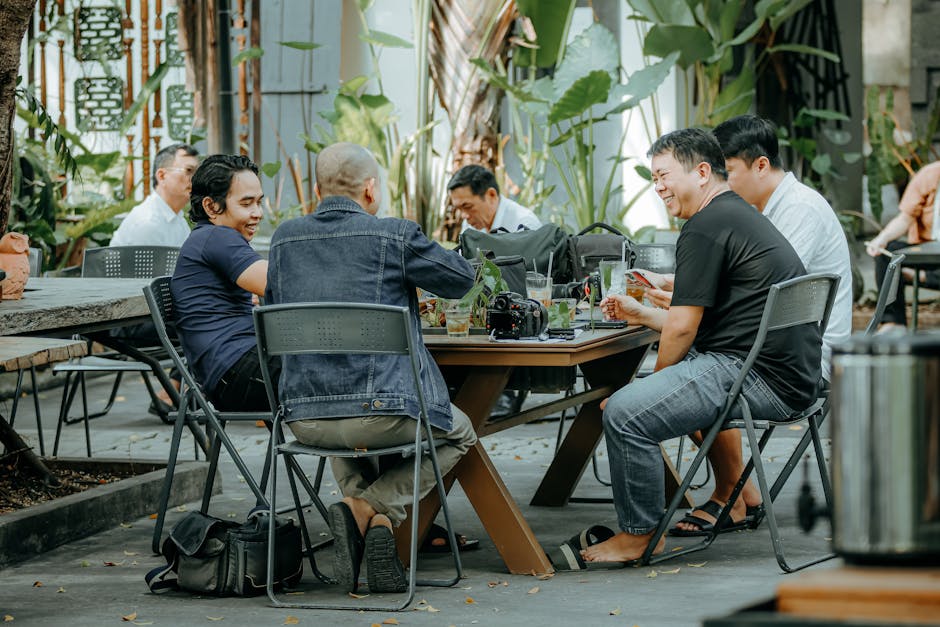 Men having a casual meeting outdoors at a café with greenery around them.