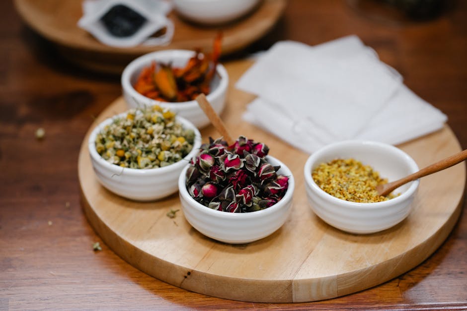 Close-up view of various dried herbs and spices in white bowls on a wooden tray, perfect for culinary arts or natural remedies.