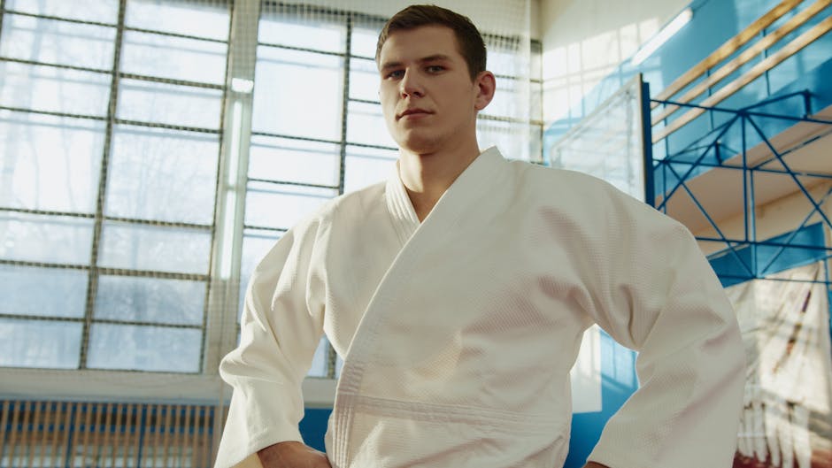Confident young male athlete wearing a judo uniform inside a bright gym.