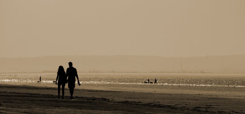 Silhouette of a couple walking hand in hand along a serene beach at sunset, capturing a romantic and tranquil moment.