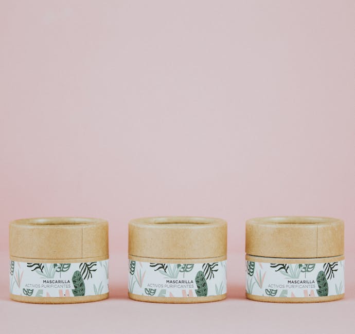 Three eco-friendly cosmetic jars with botanical labels against a pink backdrop.