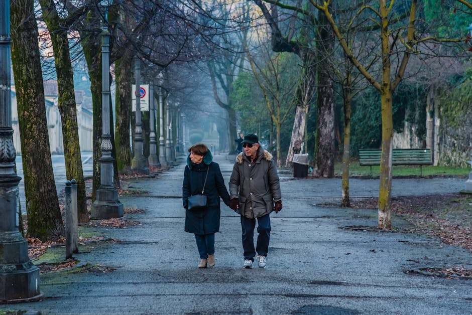 Elderly couple strolls hand in hand through a serene park in Italy, capturing a moment of togetherness.
