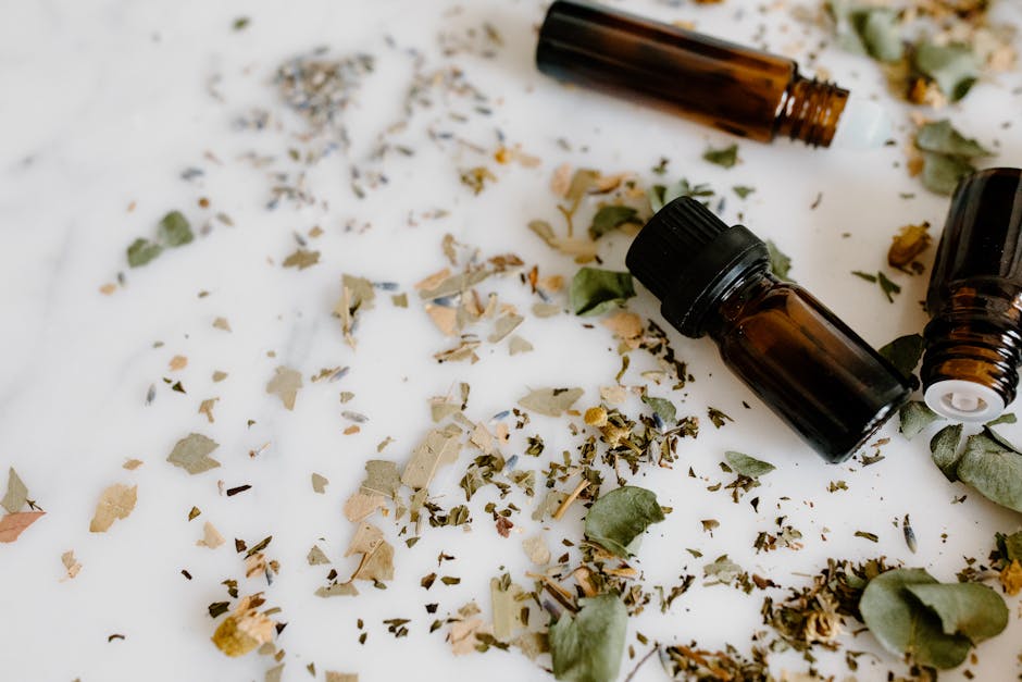Aromatherapy setup with essential oil bottles and dried herbs on a white surface for holistic healing.