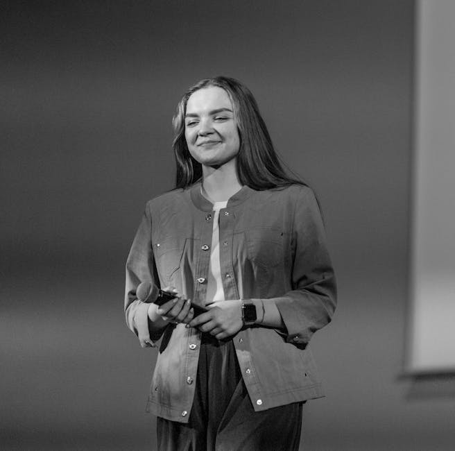 Caucasian woman smiling while holding a microphone, captured in artistic grayscale.