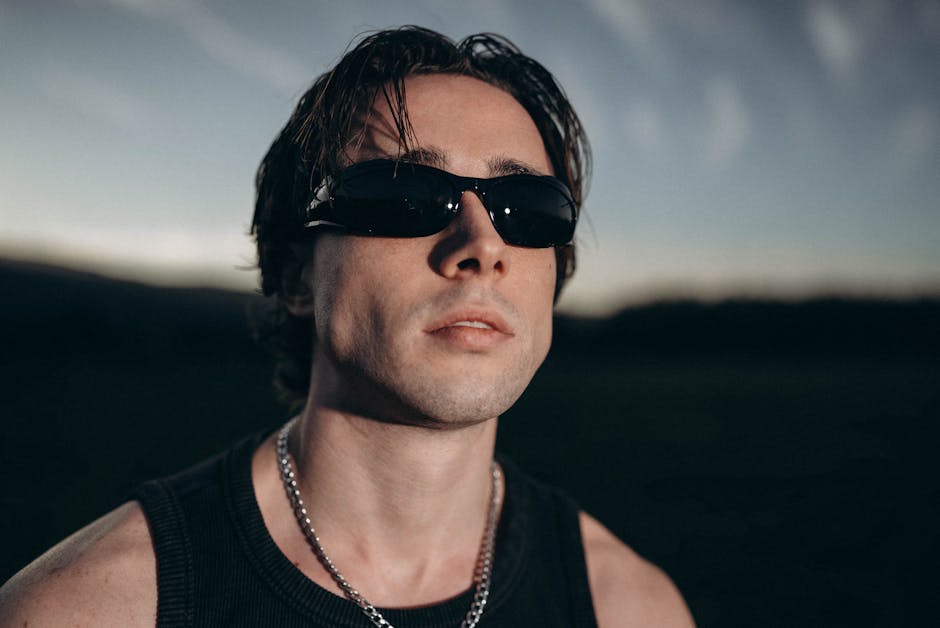 Portrait of a stylish man wearing sunglasses and a chain necklace, captured during sunset outdoors.