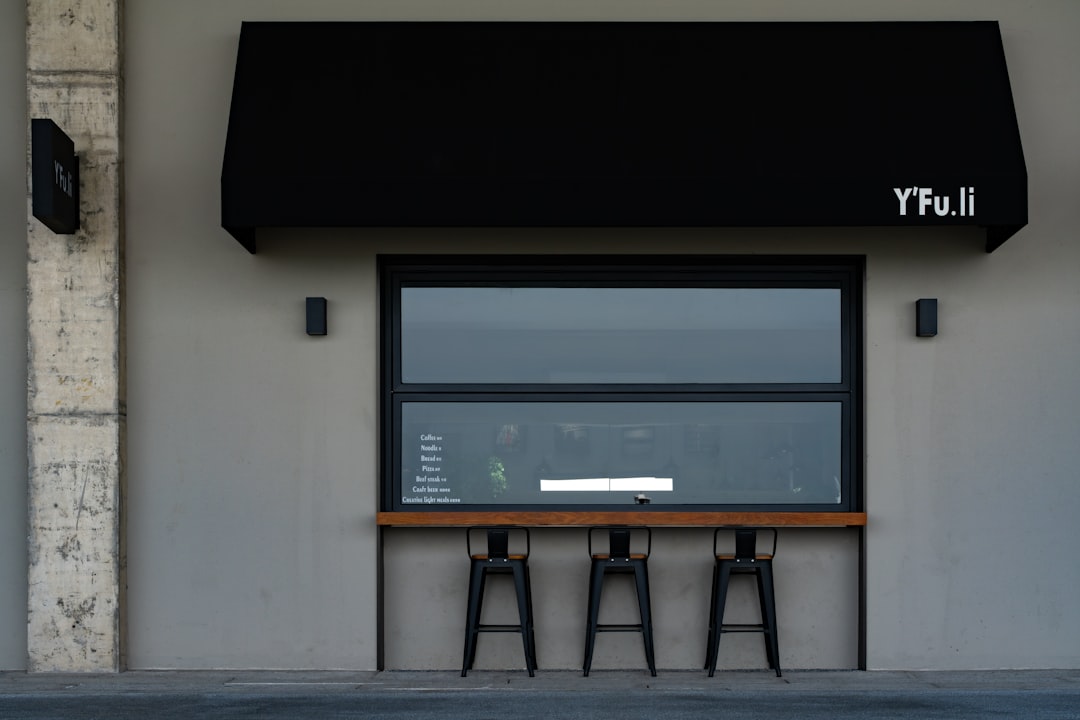 A modern shopfront with stools and a black awning.
